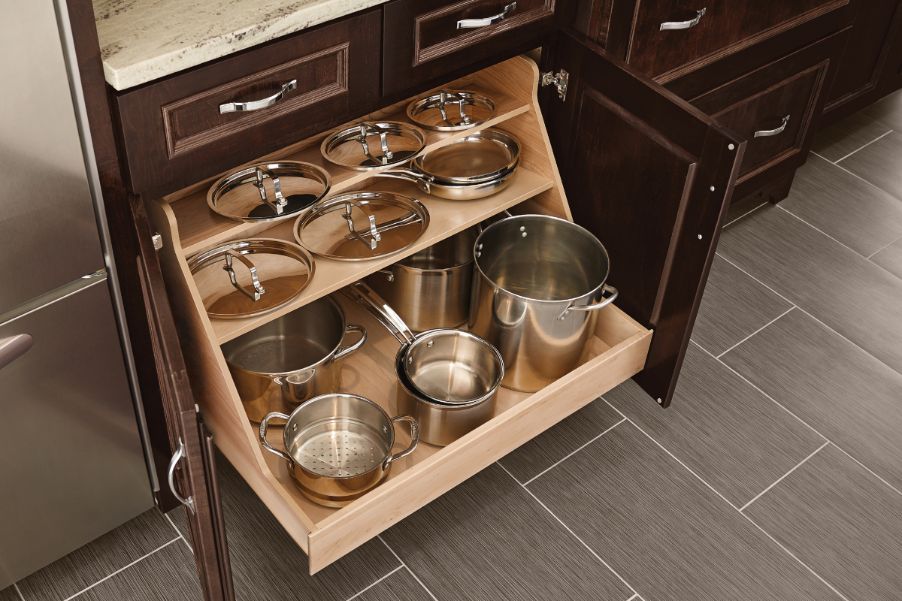 Open doors of a traditional-style kitchen base pots and pans organizer roll-out cabinet to show KraftMaid wood storage organizer for pots and lids extended out for easy accessibility
