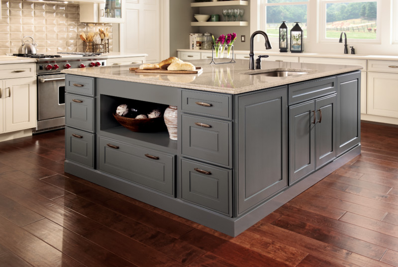 Kitchen island with stone countertop and prep sink atop painted KraftMaid cabinets